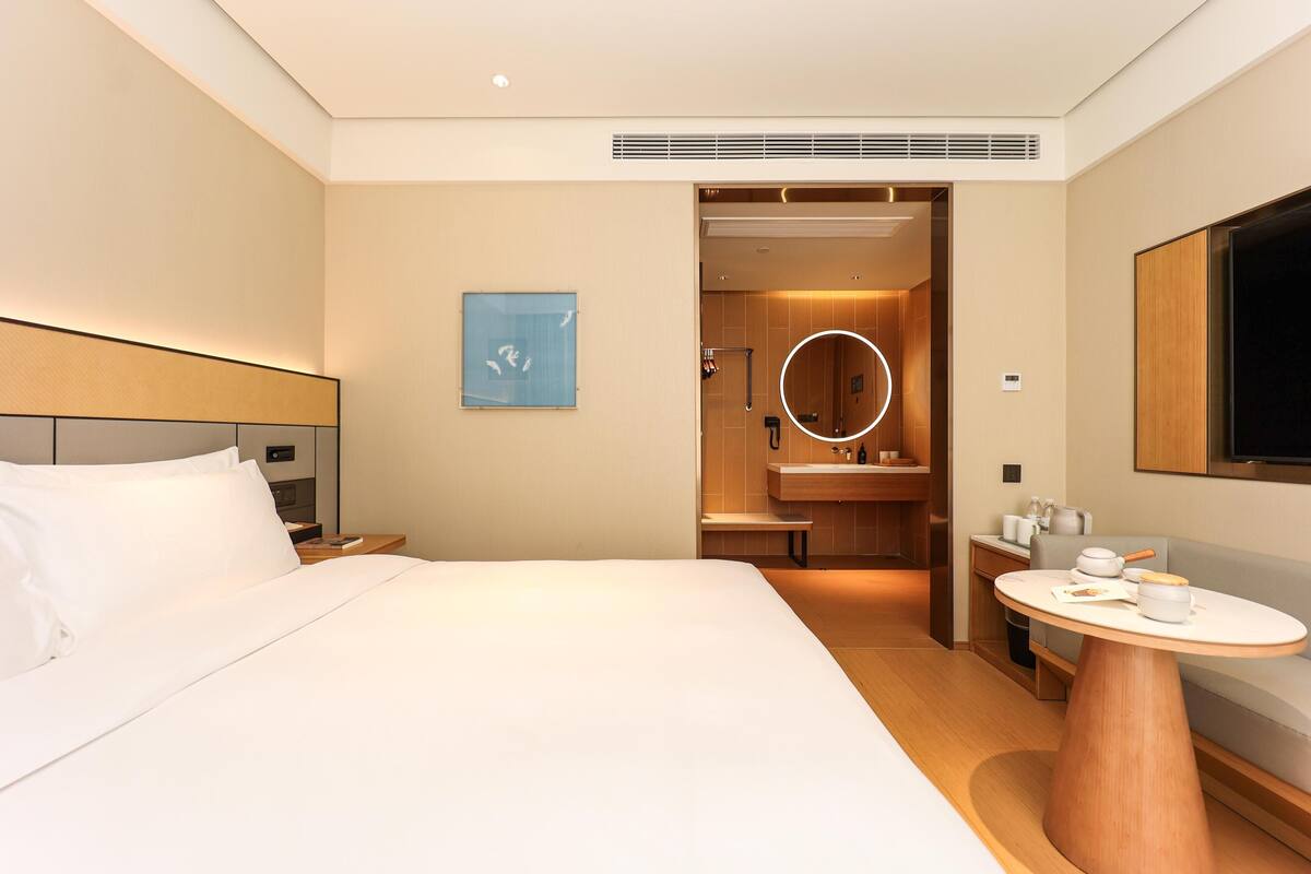 A hotel room with a bed, a round mirror, a small table, and a TV.