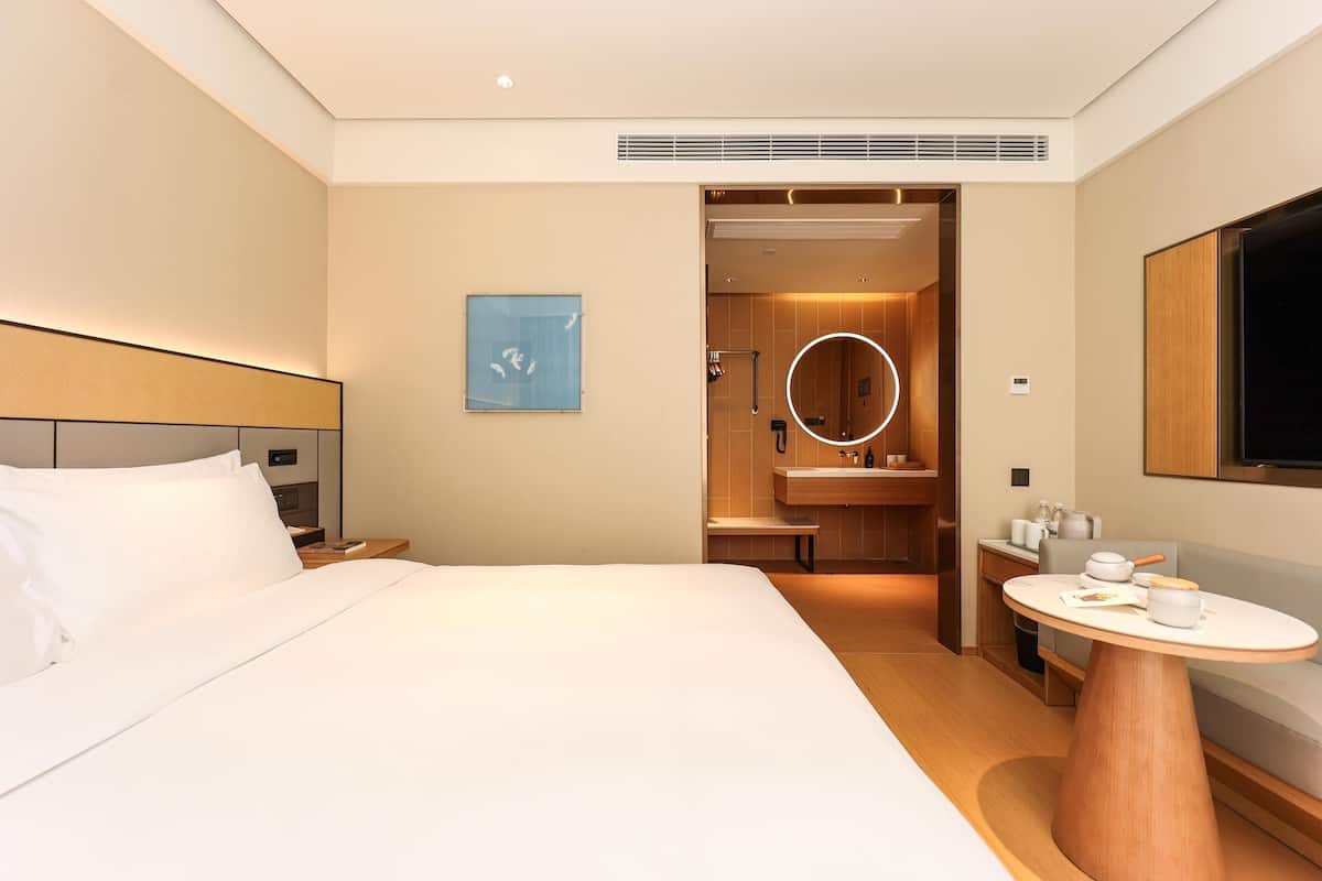 Quarto de hotel com cama, espelho redondo, mesa pequena e televisão.