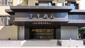 L’entrée d’un hôtel, avec une façade moderne, de grandes portes vitrées et un escalier en béton menant à l’entrée.