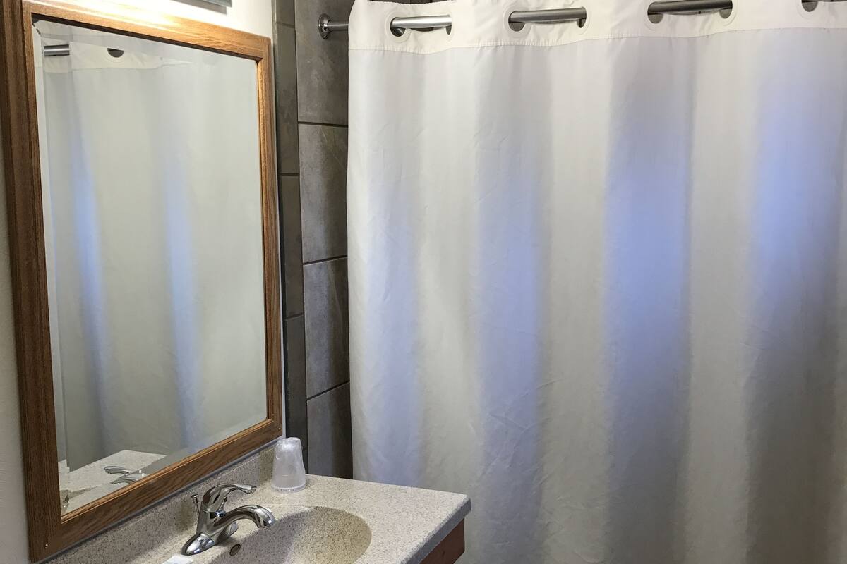 A bathroom with a granite countertop sink, a wooden vanity, a large mirror, and a shower curtain.