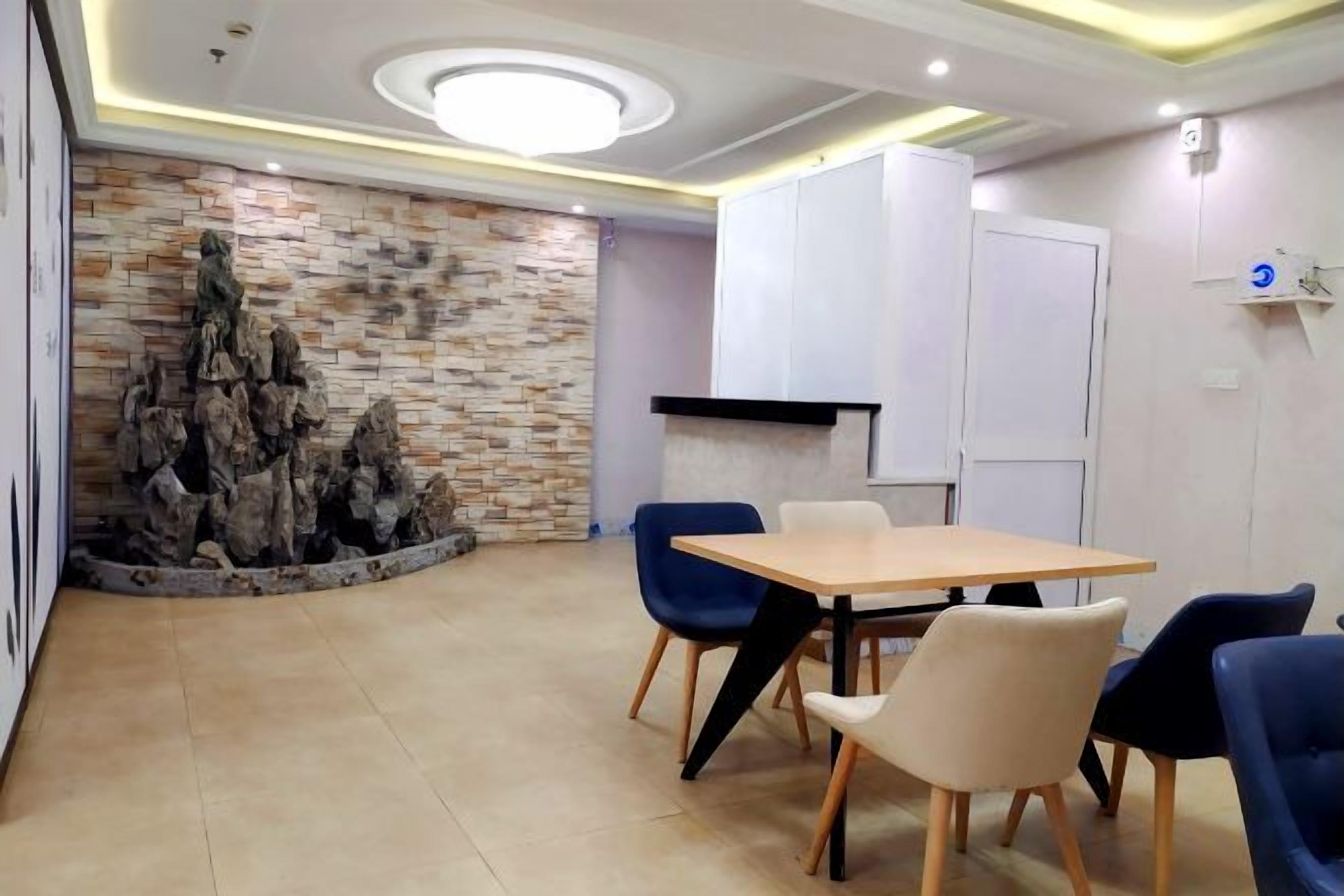 Sala de conferências com mesa de madeira, cadeiras azuis e brancas, parede de pedra e iluminação embutida no teto.