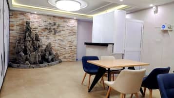 Sala de conferências com mesa de madeira, cadeiras azuis e brancas, parede de pedra e iluminação embutida no teto.