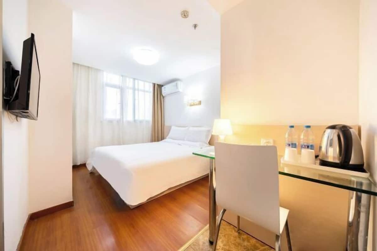 Une chambre d’hôtel comprenant un lit, un bureau avec une chaise, une télévision et une fenêtre avec des rideaux.
