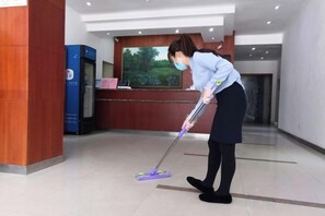 Une personne nettoie un hall d'entrée à l'aide d'une serpillière et d'un seau.