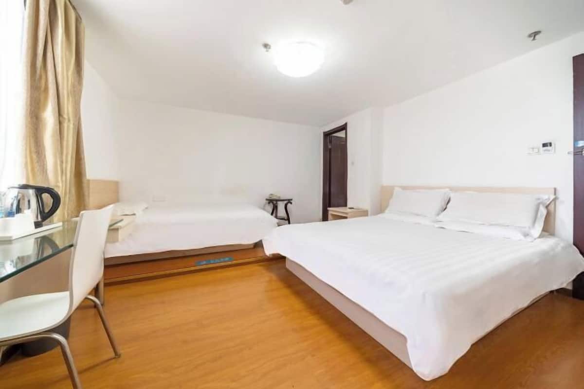 Une chambre d’hôtel avec deux lits simples, un bureau avec une chaise, une petite table et une table de chevet.