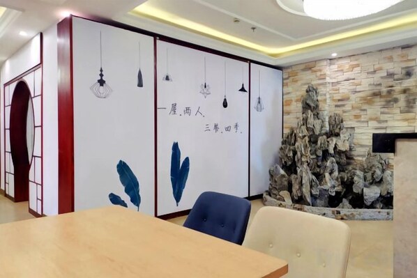 A conference room with a wooden table, chairs, a decorative wall with calligraphy, and a stone wall with a rock formation.