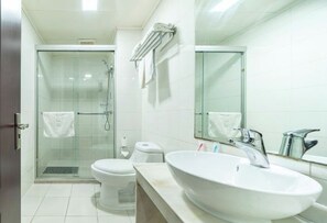 Een moderne badkamer met een douchecabine van glas, een wit toilet, een groot wastafelmeubel met spiegel en een handdoekrek.