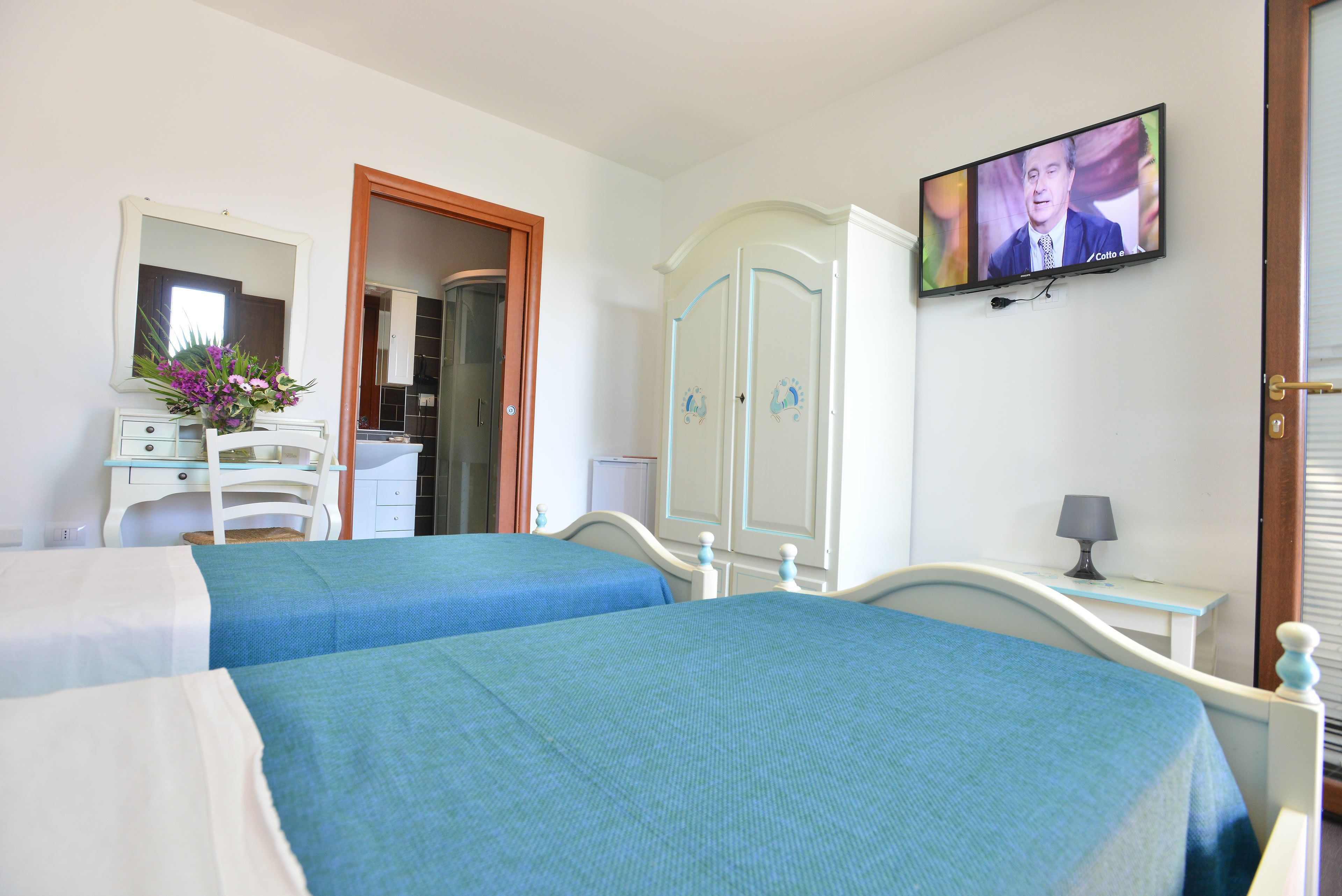 Habitación de hotel con dos camas, televisión, espejo, armario y escritorio con lámpara.
