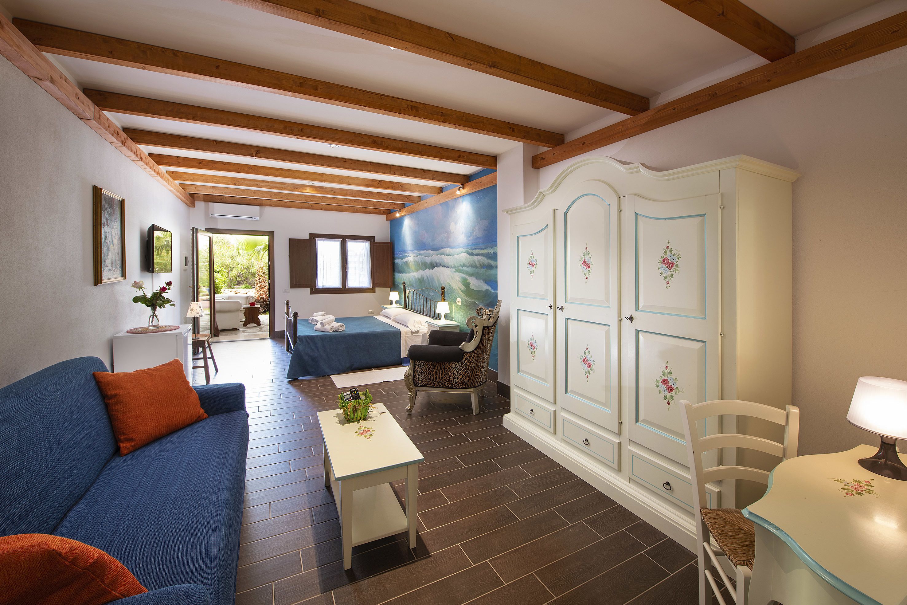 A room with a blue sofa, a white table, a patterned armchair, and a cabinet with floral decorations.