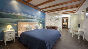 Ein Schlafzimmer mit einem großen Bett, einem Nachttisch mit Lampe, einem Sessel, einem Schreibtisch und einem Spiegel.