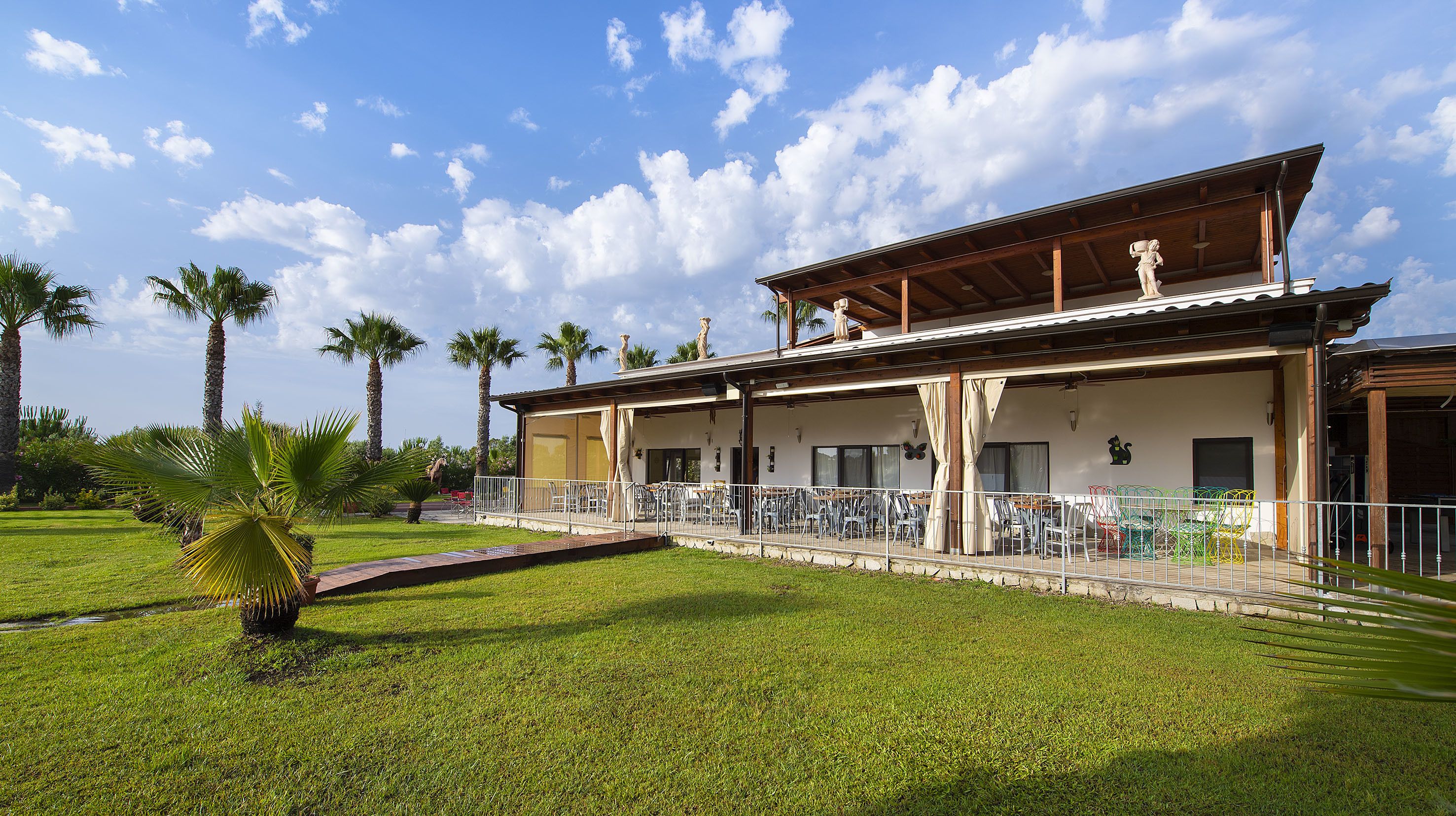A two-story building with a covered patio area, palm trees, and a clear sky.