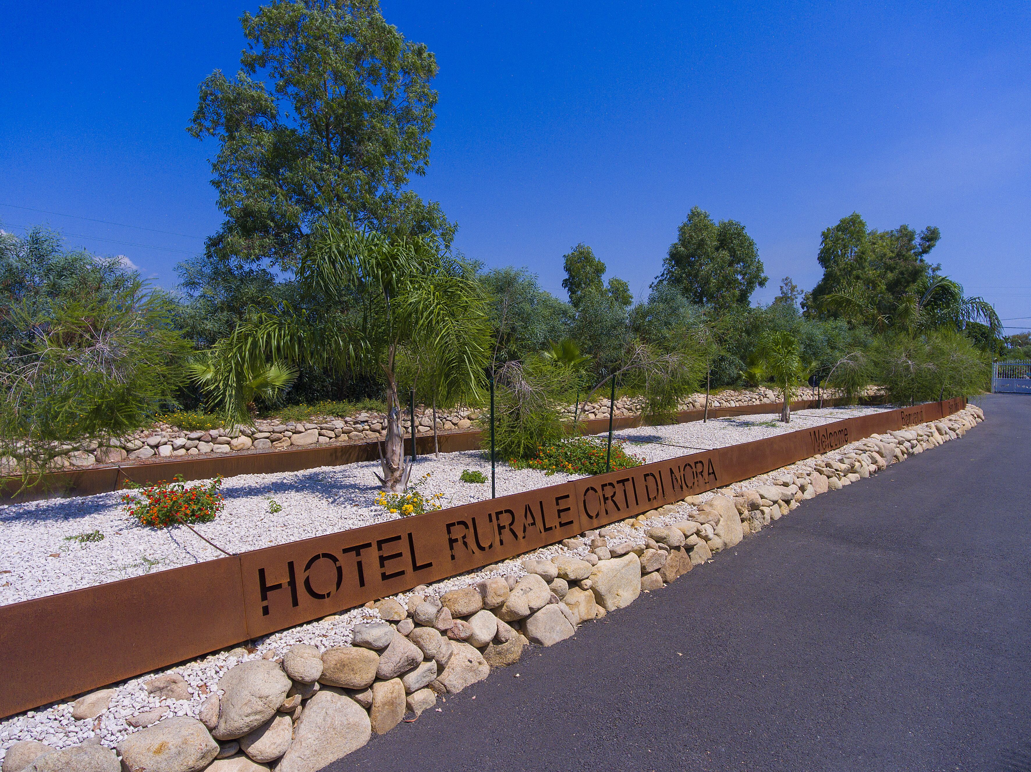 Une enseigne indiquant « HÔTEL RURAL DI NORA », avec un chemin de gravier et des rochers.