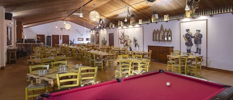 A billiards hall with multiple tables and chairs, wooden ceiling, and wall-mounted decorations.
