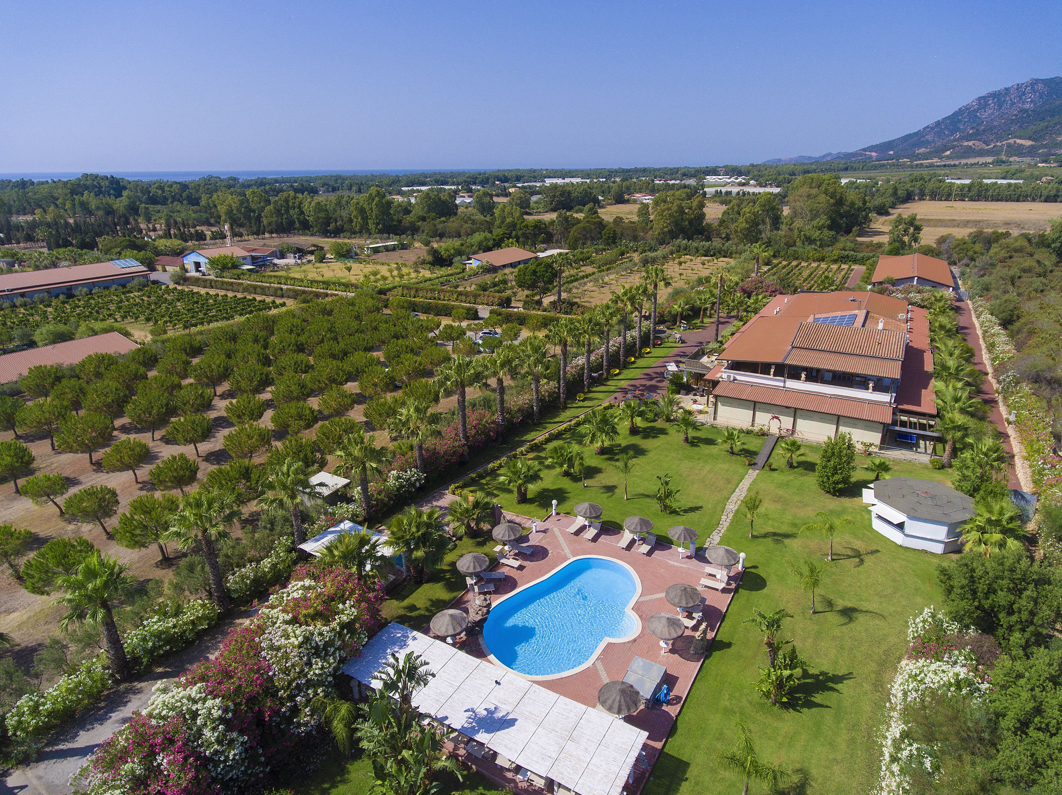 An aerial view of a resort with a swimming pool, landscaped gardens, and a view of the surrounding landscape.