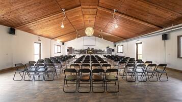 Ein großer Saal mit in Reihen angeordneten Stühlen, Holzboden und natürlichem Licht durch Fenster.