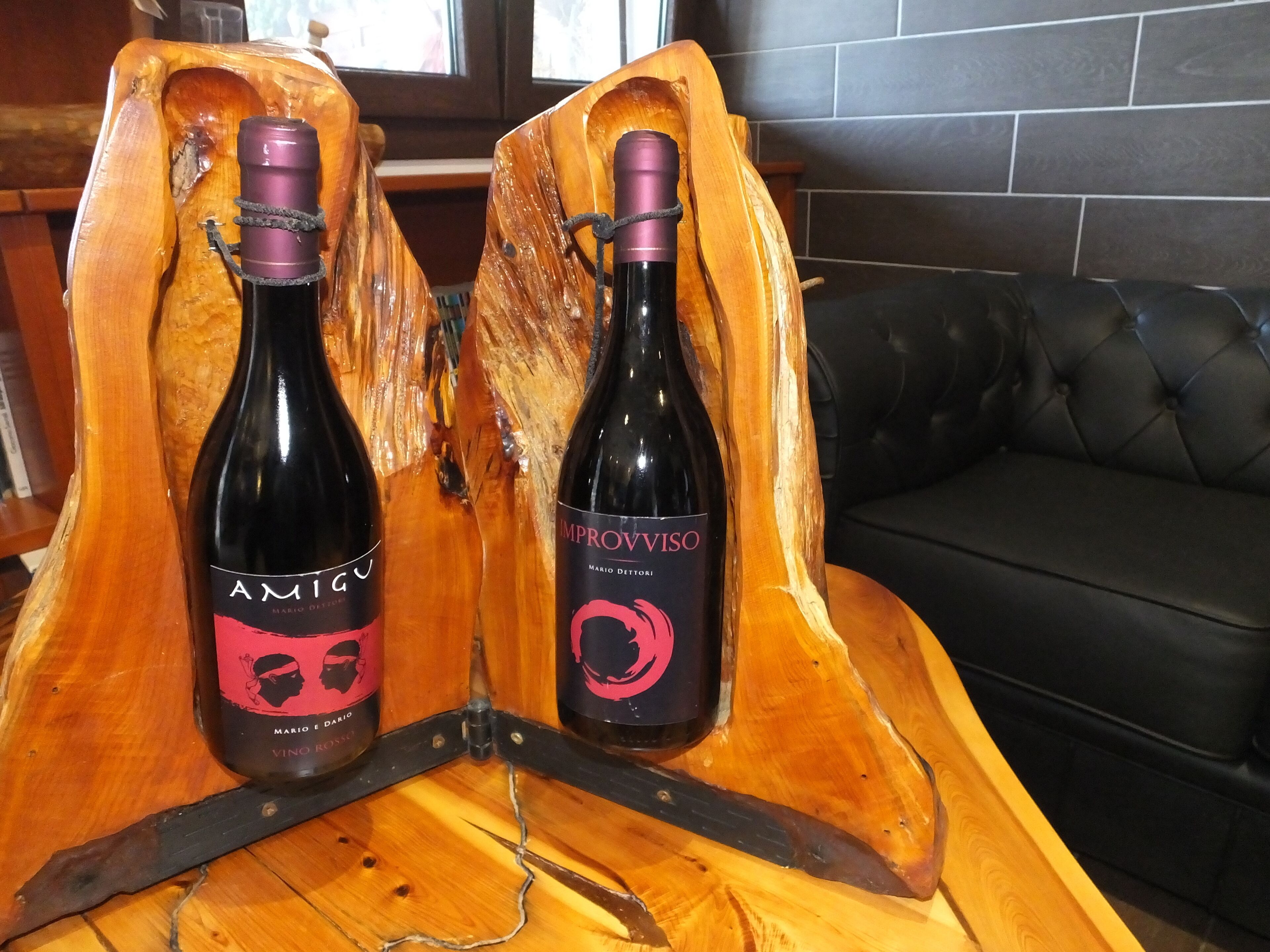 Two wine bottles on a wooden stand in a room with a black leather couch.