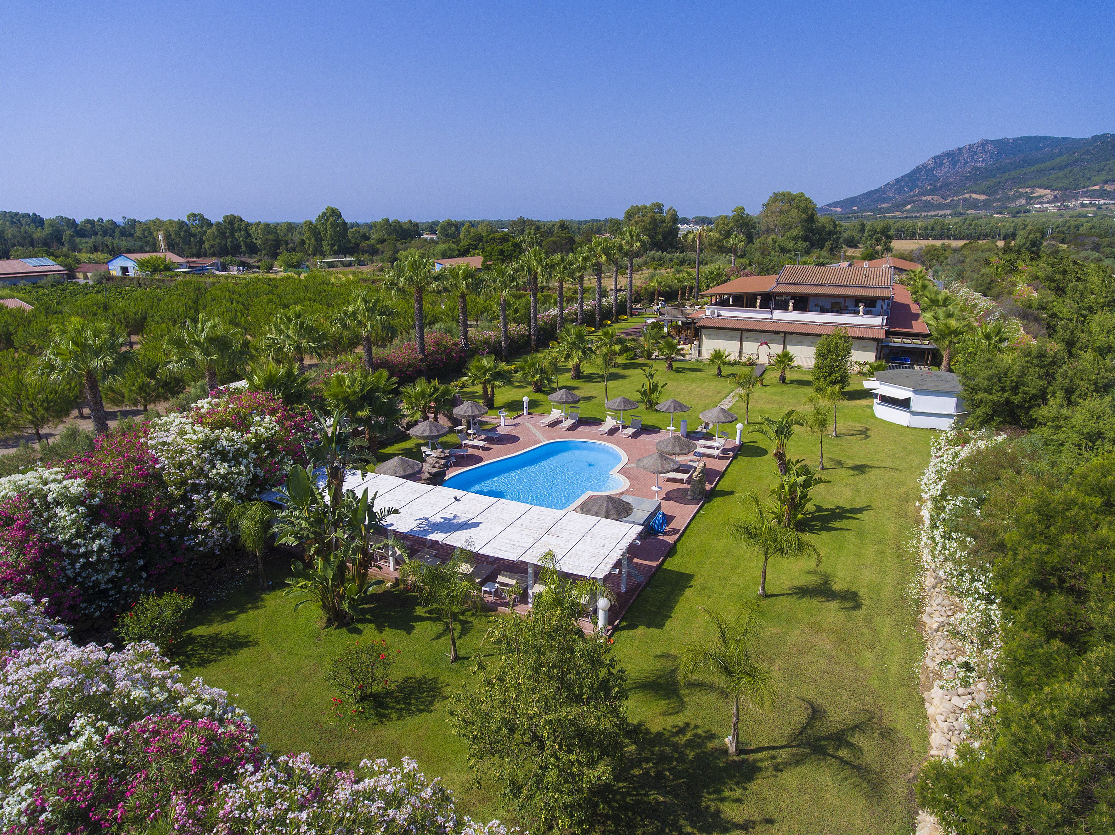 A resort with a swimming pool, lounge chairs, and a large house with a red roof.