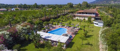 A resort with a swimming pool, lounge chairs, and a large house with a red roof.