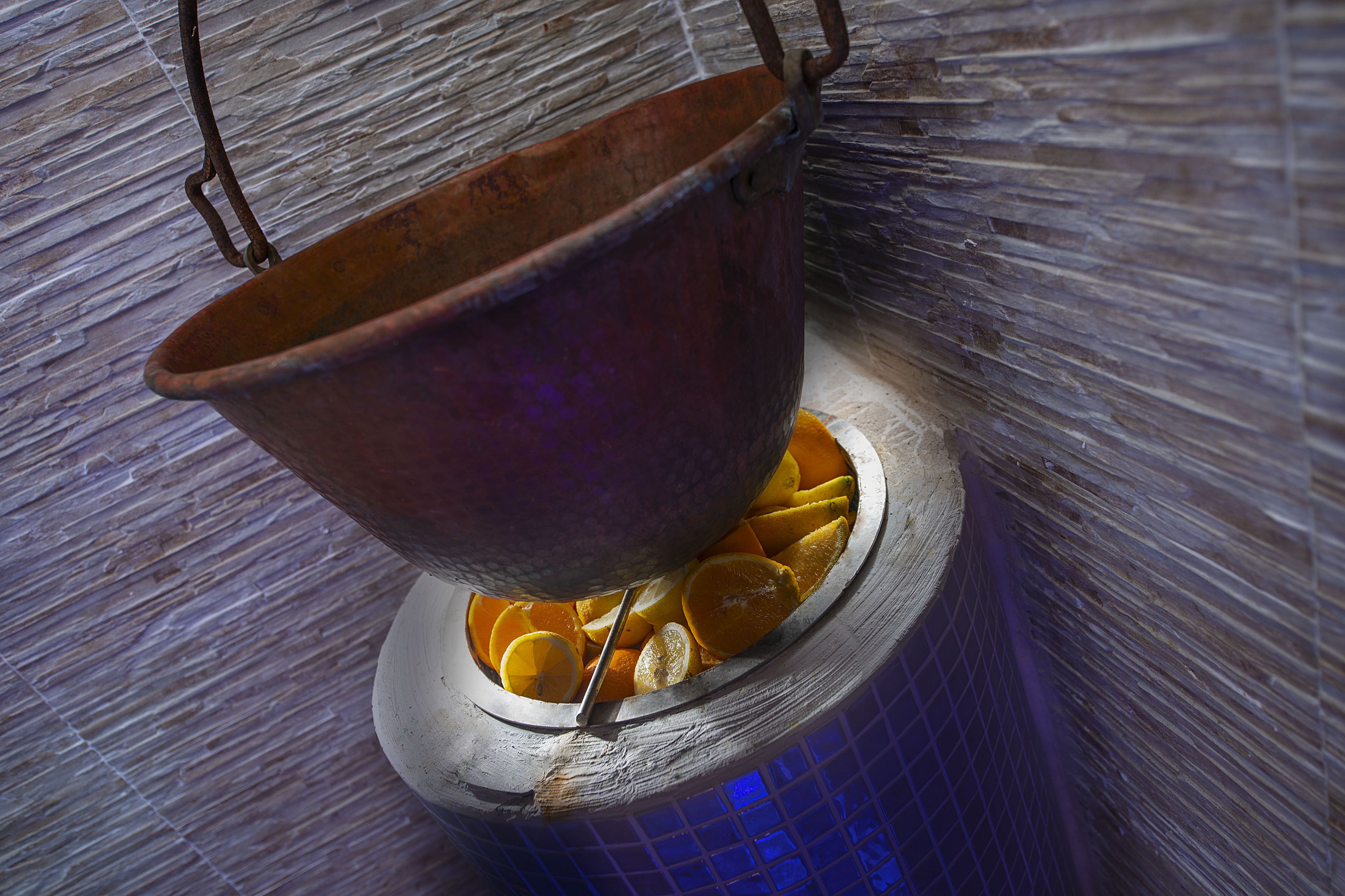 A copper pot with oranges inside, placed on a tiled surface.