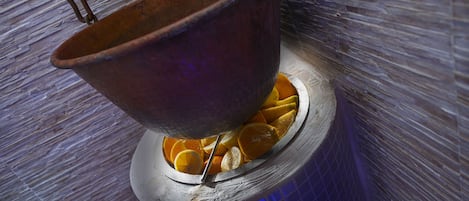 A copper pot with oranges inside, placed on a tiled surface.
