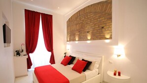 A bedroom with a large bed, red curtains, a brick-patterned wall, a mounted TV, and bedside lamps. - Guest house Interno 7 Luxury Rooms (Rome)
