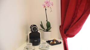 A small table with a coffee maker, two cups, a tray of chocolates, a potted plant, and a red curtain. - Guest house Interno 7 Luxury Rooms (Rome)