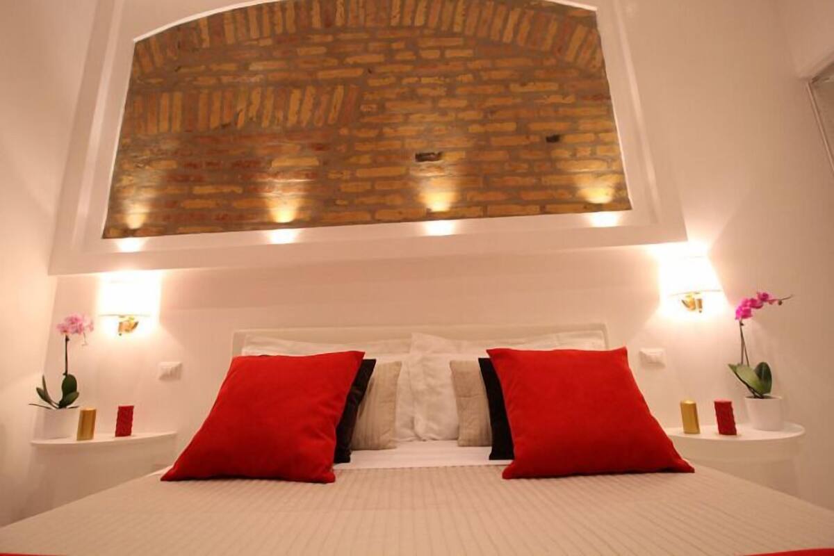 A bedroom with a brick-patterned ceiling, white bedding, and red pillows.