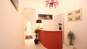 A reception area with a red counter, a chandelier, framed pictures, and potted plants. - Guest house Interno 7 Luxury Rooms (Rome)