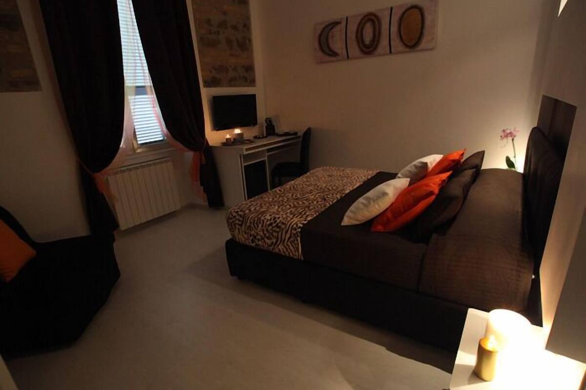 A bedroom with a bed, a desk, and a window with curtains.