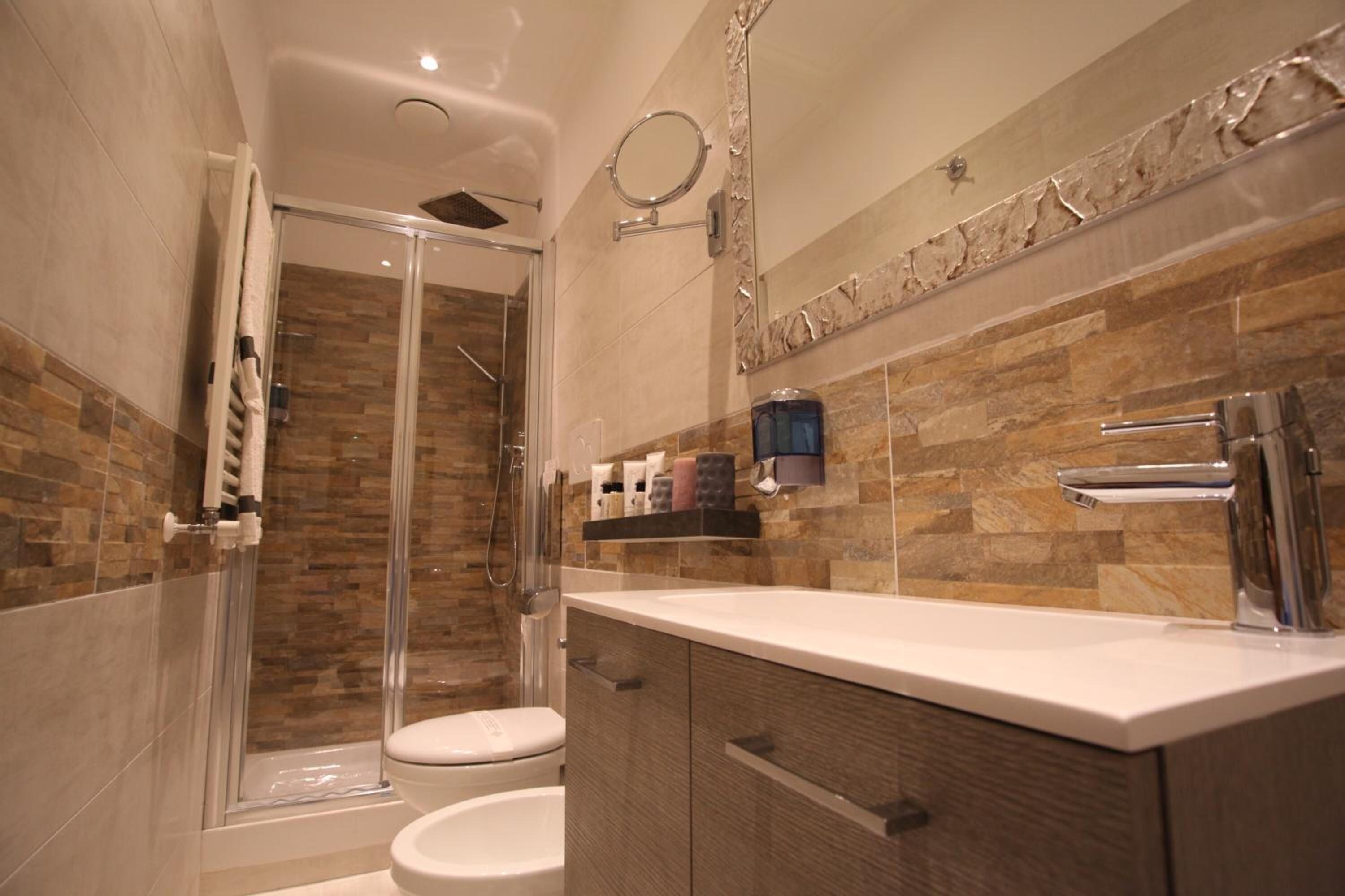 A modern bathroom with a glass-enclosed shower, a white toilet, and a vanity with a mirror and a shelf of toiletries.