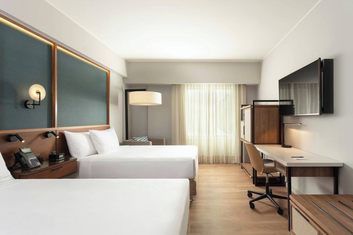 A hotel room with two beds, a desk, a chair, a TV, a lamp, and a phone on the nightstand.