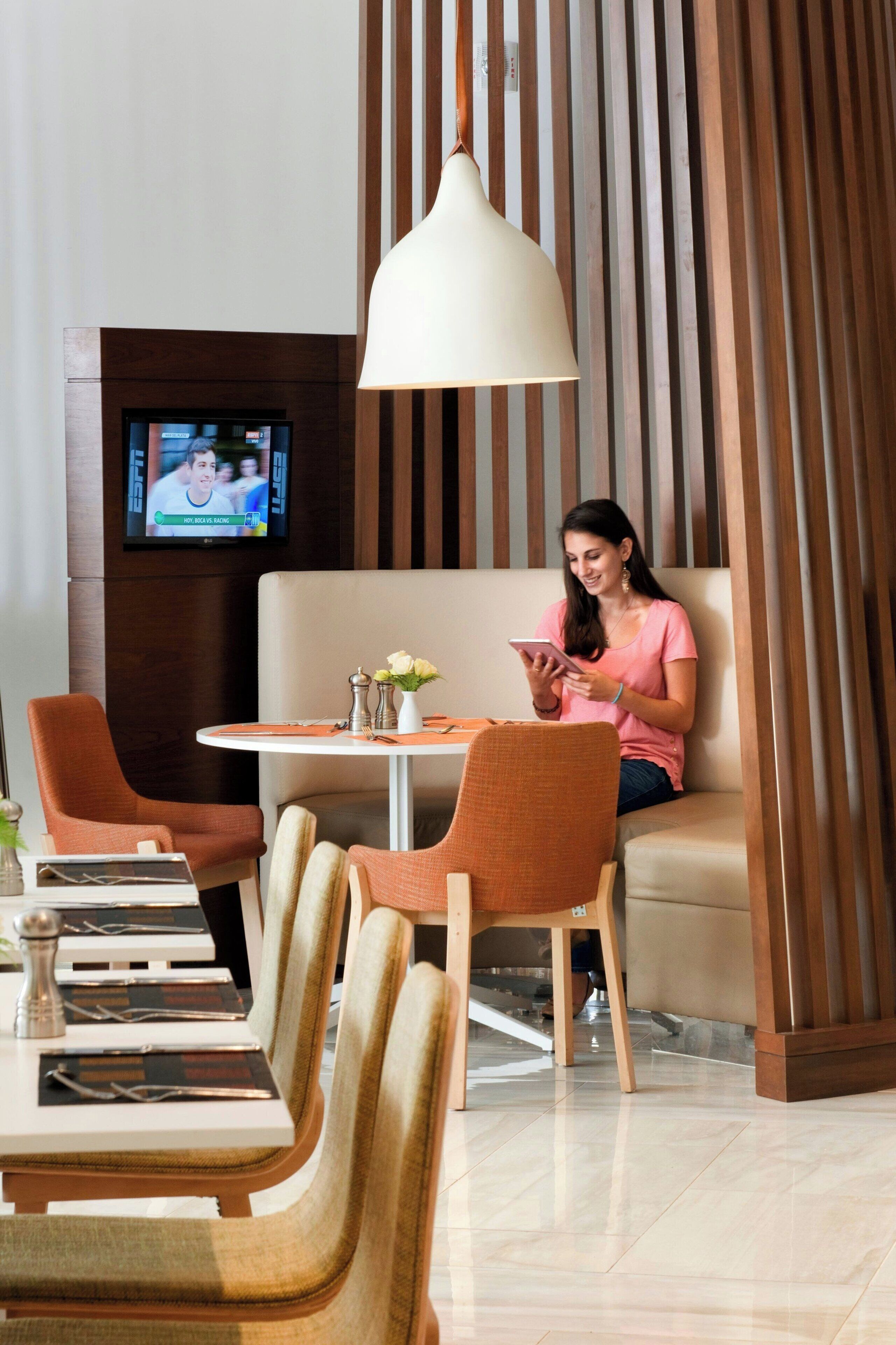 Un hall d’hôtel moderne avec un coin salon, un téléviseur et une table agrémentée d’un vase de fleurs.