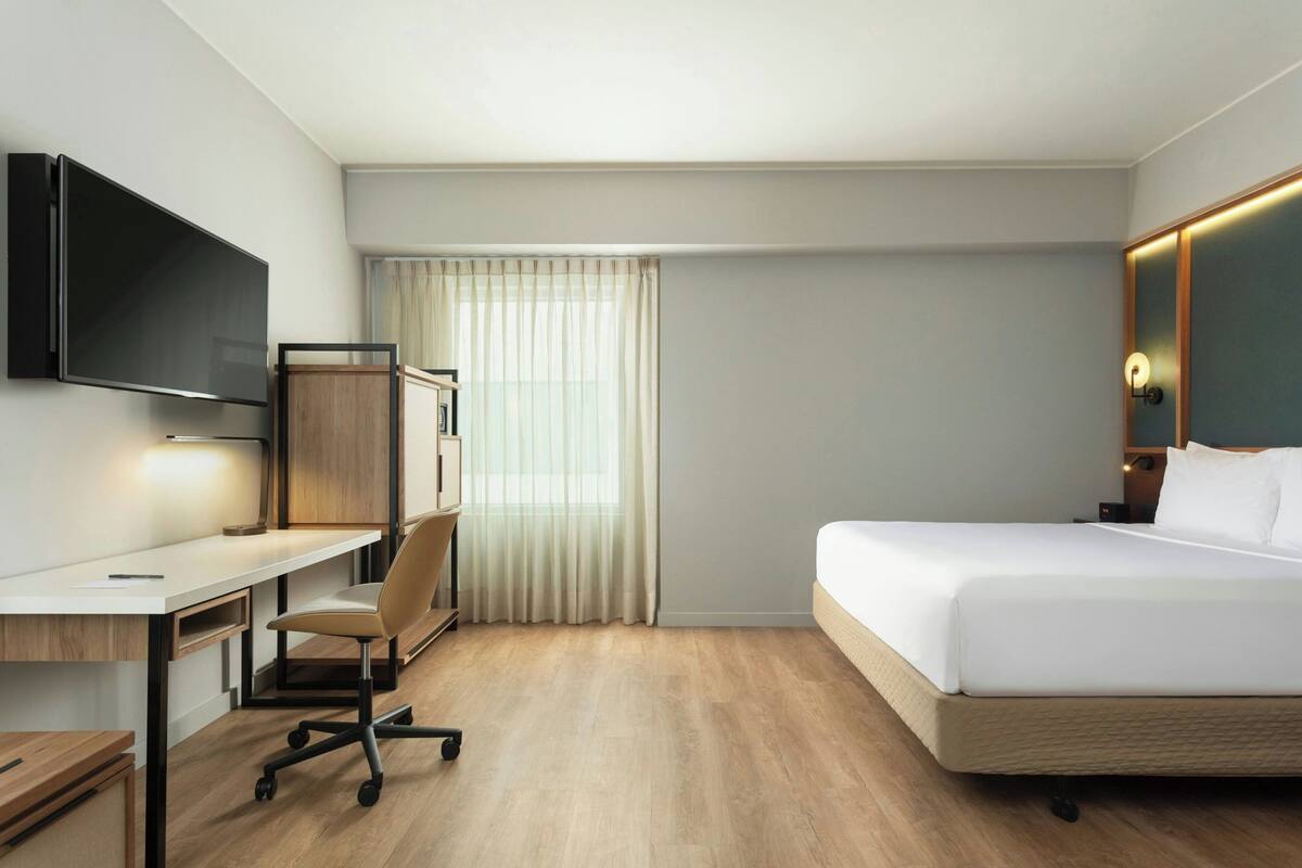 A hotel room with a bed, a desk, a chair, a television, and a window with curtains.