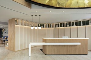 Un mostrador de recepción moderno con acabado de madera y una encimera blanca. Tres lámparas colgantes iluminan el mostrador, y hay una placa con el nombre encima.