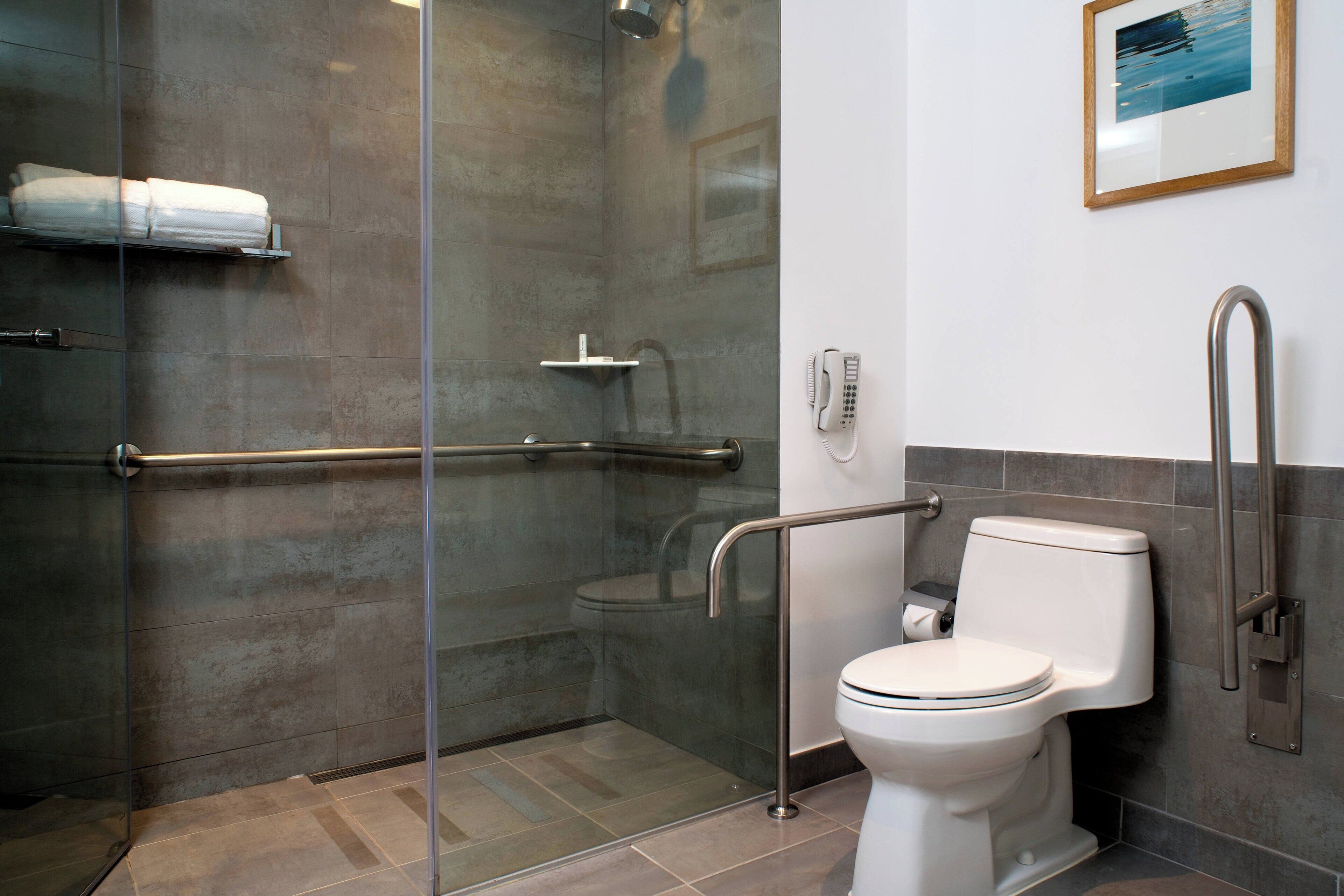 A modern bathroom with a glass-enclosed shower, a white toilet with a grab bar, and a mounted phone.