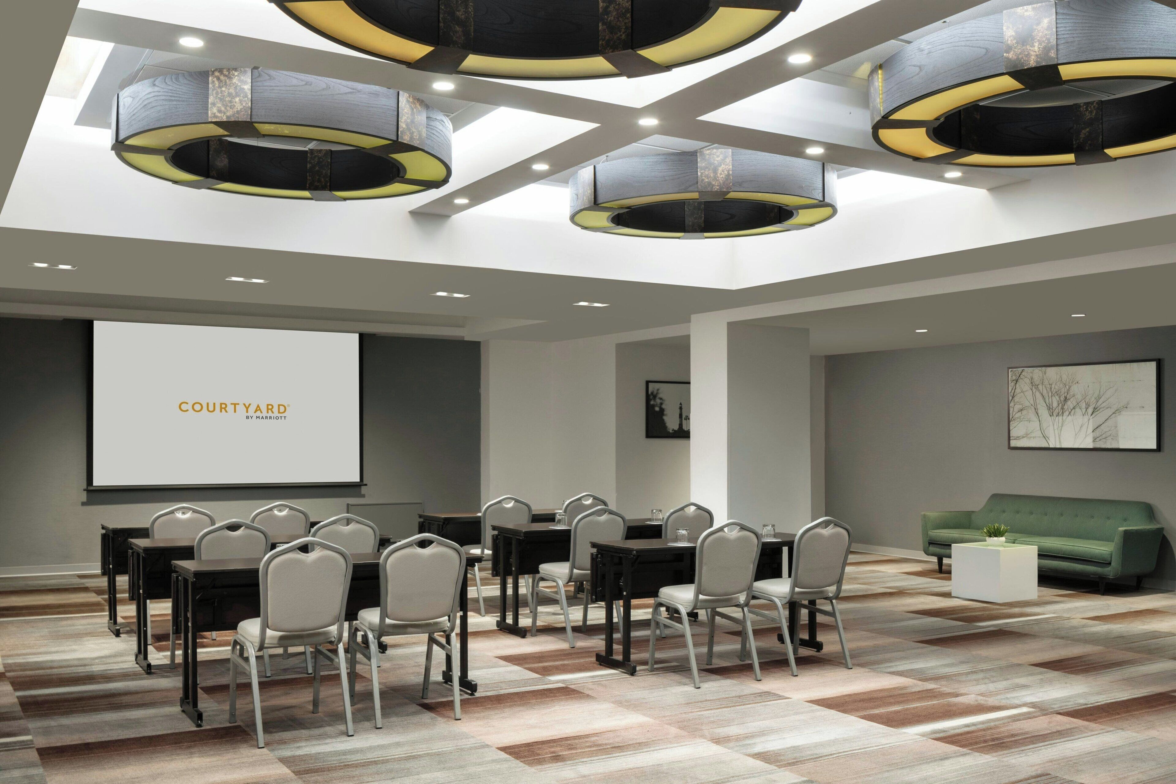 A conference room with a large screen displaying "COURTYARD by Marriott," a green sofa, and a patterned floor.