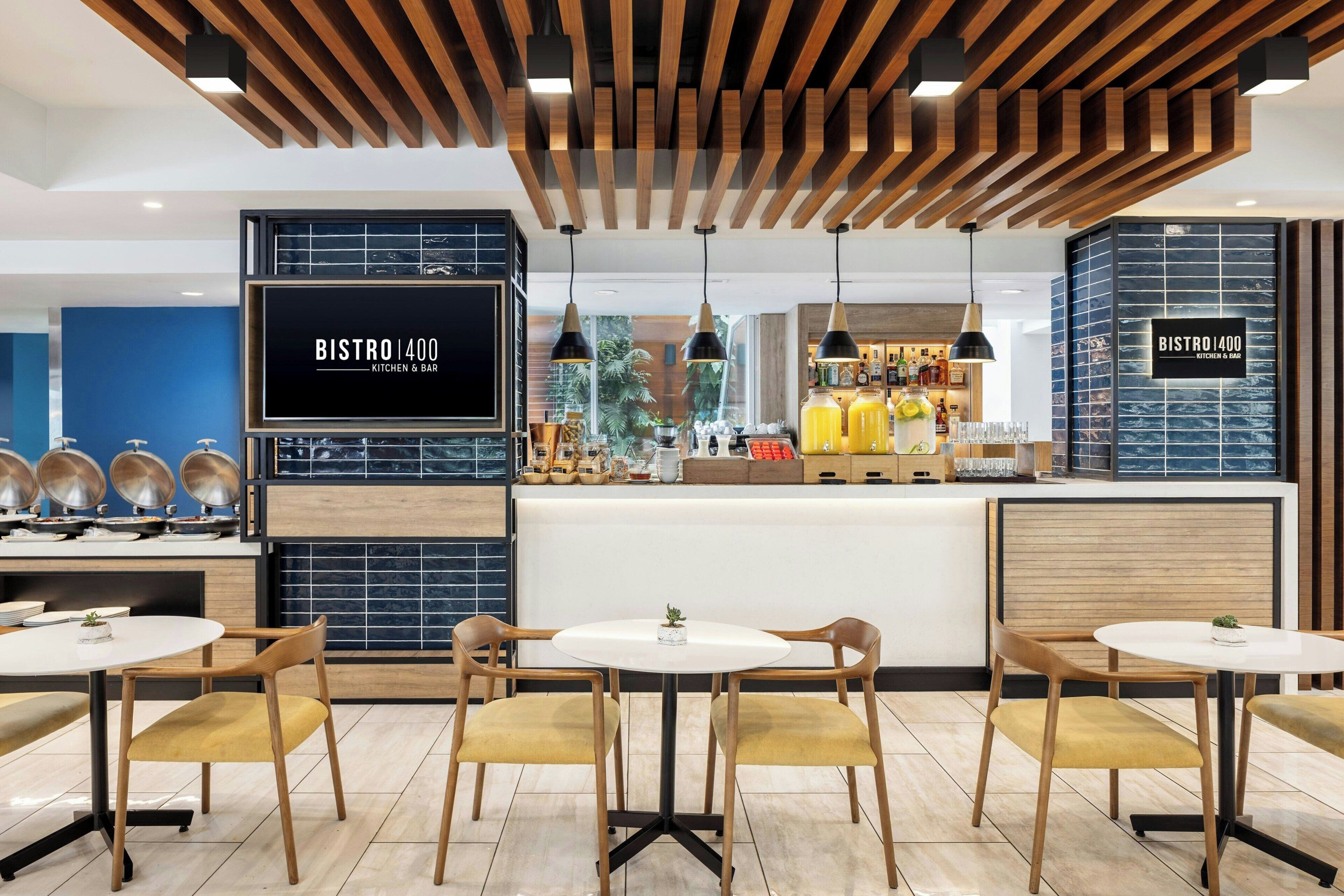 Un bistró moderno con techo de madera, una isla central con equipo de cocina y zonas de estar con mesas y sillas redondas.