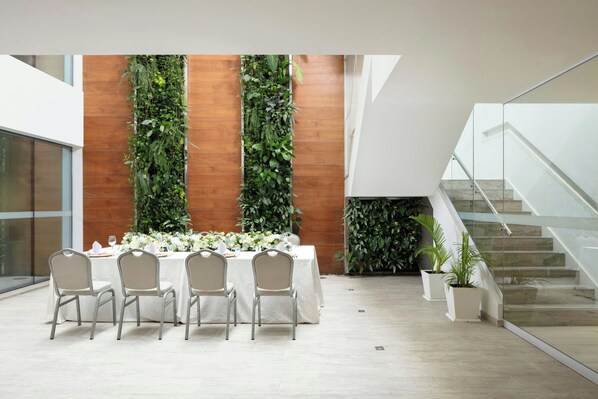 A modern indoor space with a long table set for a meal, surrounded by chairs, and a vertical garden wall.