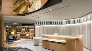 A modern hotel reception area with a wooden reception desk, seating area with a sofa and chairs, and a wall with decorative vases. - Courtyard by Marriott Lima Miraflores (Lima)