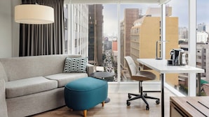 A modern living room with a sofa, ottoman, and a desk with a chair. There is a large window offering a city view. - Courtyard by Marriott Lima Miraflores (Lima)