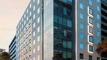 Un hotel moderno con fachada de vidrio, varios pisos y entrada a través de un patio.