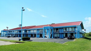 Un motel con techo rojo y paredes exteriores azules, que cuenta con varios balcones y un estacionamiento.