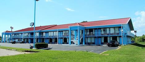 A motel with a red roof and blue exterior walls, featuring multiple balconies and a parking lot.