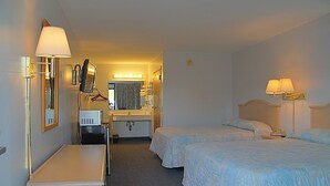 Habitación de hotel con dos camas, un escritorio con computadora, un espejo y tocador con lavamanos.
