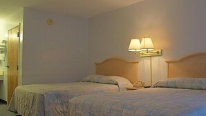 Una habitación de hotel con dos camas, una mesita de noche y una lámpara de pared.