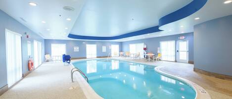 An indoor swimming pool with clear water, a lifebuoy, and a sign indicating a depth of 1.5 meters.