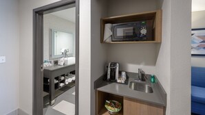 Ein kleines Badezimmer mit Spiegel, Waschbecken, Mikrowelle und Kaffeemaschine.