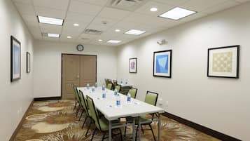 A conference room with a long table, chairs, water bottles, framed pictures on the walls, and a clock.