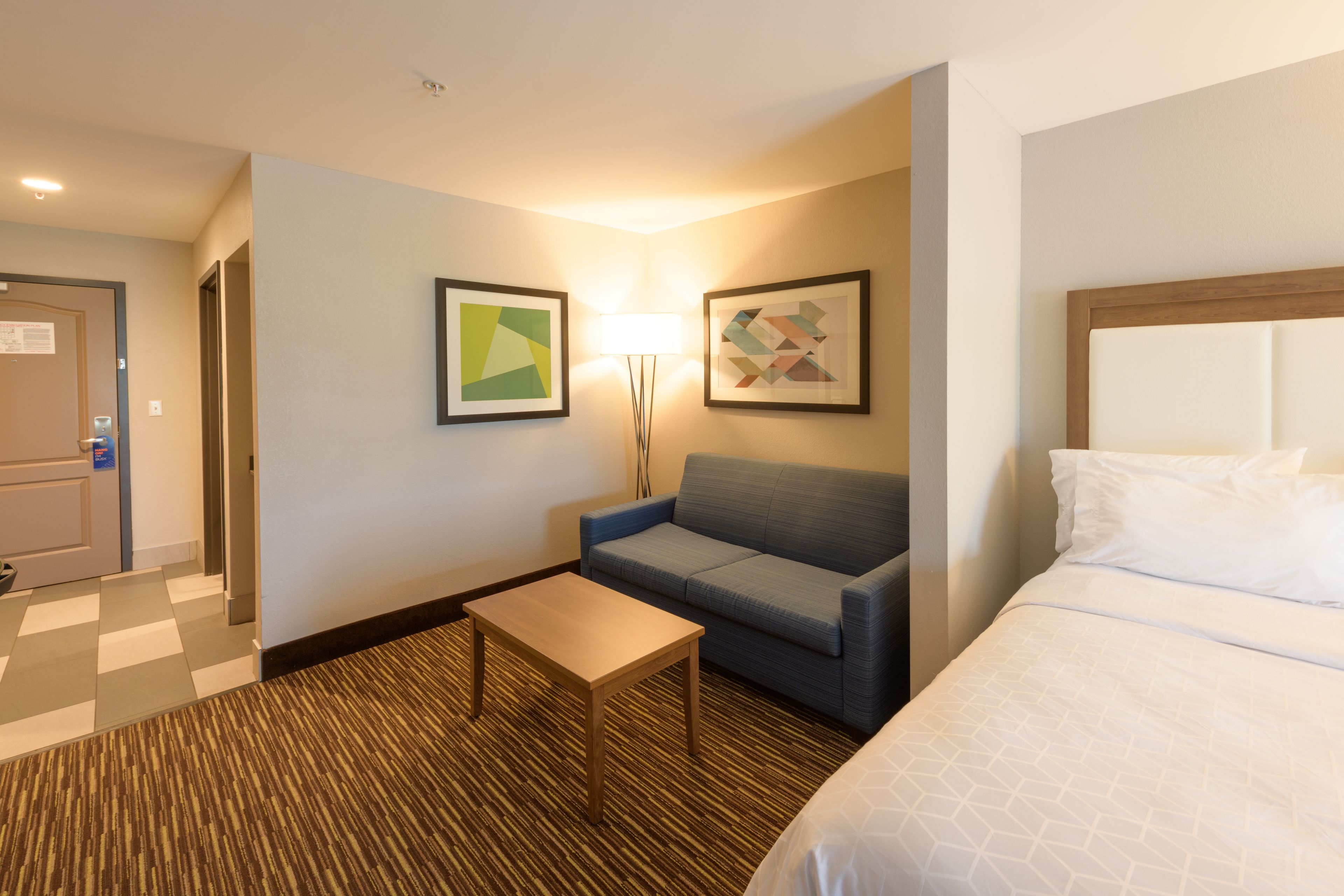 A hotel room with a bed, a sofa, a small table, and two framed artworks on the wall.