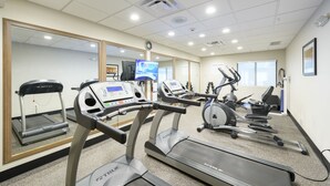 Ein Fitnessstudio mit Laufbändern, Crosstrainern und einer Spiegelwand.